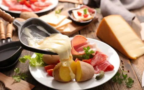 Roztopiony ser z patelni do raclette spływa na ziemniaki i wędliny. Pyszne danie raclette.
