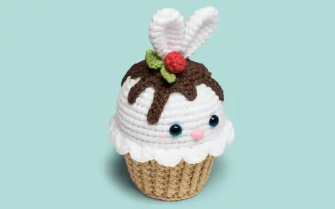 Adorable cupcake amigurumi con orejas de conejo, glaseado blanco, chispas de chocolate y una cereza. ¡Un dulce amigo tejido!