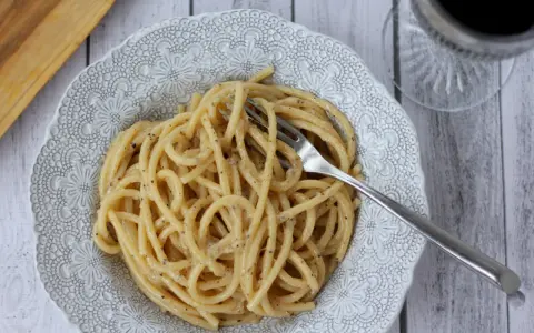 Porcja pysznego cacio e pepe na ozdobnym talerzu, z widelcem w makaronie.