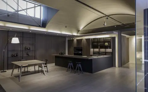 Moderna cocina office con isla central, muebles oscuros, estanterías y mesa de comedor.