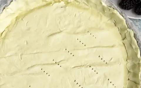 Surowe ciasto na tartę, z widocznymi dziurkami, czeka na wypełnienie. Tarta na kruchym spodzie czy na cieście francuskim?