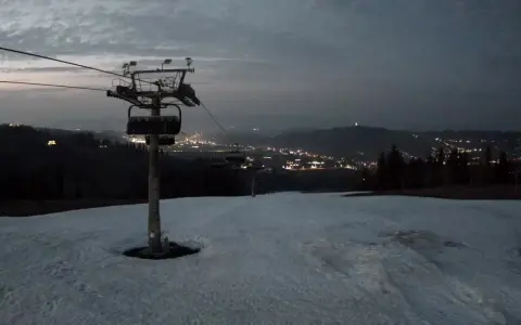 Widok z bukowina ski kamery na ośnieżony stok i nocne światła miasta w oddali.