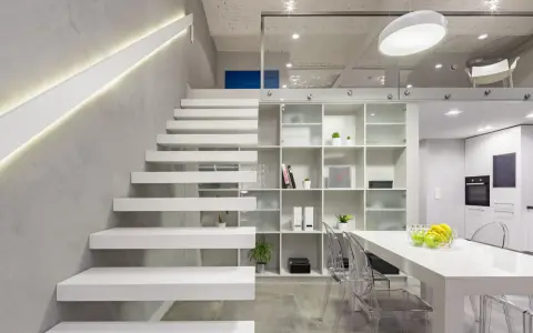 Nowoczesna antresola z białymi, lewitującymi schodami, przeszklonymi balustradami i minimalistycznym regałem.