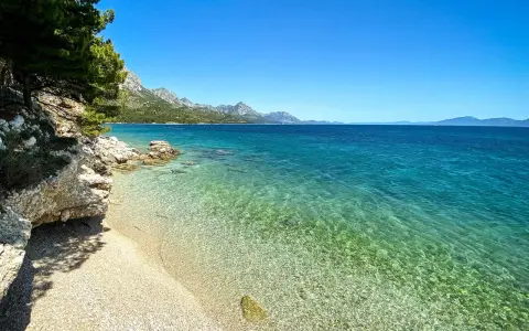 Idealne miejsce na camping w Chorwacji: kamienista plaża, turkusowa woda i góry w tle.