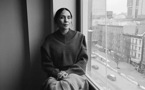 Ming Smith, a woman with her hair pulled back, sits by a window, looking out at a city street.