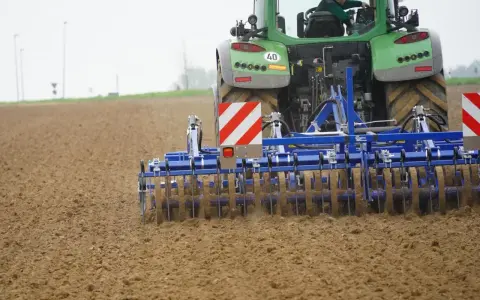Zielony traktor z agregatem uprawowym, który przygotowuje pole. Różne rodzaje wałów uprawowych pomagają w tym procesie.
