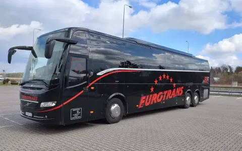 Czarny autokar turystyczny Eurotrans z czerwonymi gwiazdami i napisem na tle błękitnego nieba.