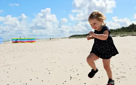 Radosna dziewczynka biega po piaszczystej plaży. Wspaniałe wakacje na Słowacji z dziećmi to marzenie każdego rodzica.