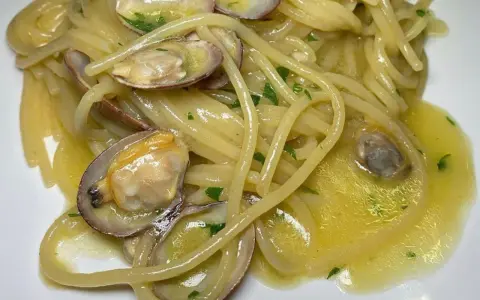 Spaghetti alle vongole cremosi come al ristorante, con vongole fresche e prezzemolo tritato su un letto di pasta dorata.