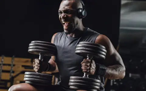Uomo con cuffie nella palestra gym, solleva pesi con musica per allenamento. Grinta e determinazione.