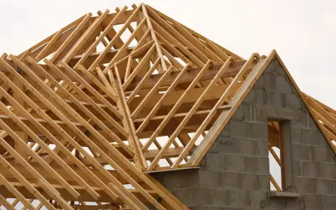 Structure en bois d'une charpente simple, en cours de construction. Les poutres de bois forment un motif complexe au-dessus des murs en blocs de béton.