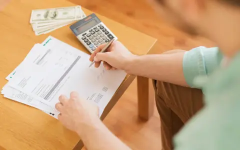 Persona revisa documentos y billetes, calculando cómo hacer un recibo de pago.