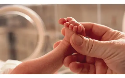Un piedino di neonato tenuto da una mano adulta. Un'immagine che evoca la delicatezza e l'importanza della valutazione Apgar, un test per valutare le condizioni del neonato alla nascita.
