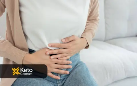 Kobieta trzyma się za brzuch, szukając odpowiedzi na pytanie, co jest dobre na jelita. Logo Keto Centrum.