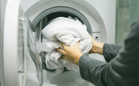 Ręce wkładają białą pościel do pralki. Zastanawiam się, jakie wirowanie w pralce będzie najlepsze dla tej delikatnej tkaniny.