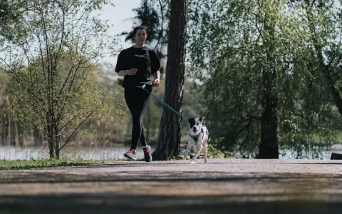 En ung kvinna och hennes hund springer längs en stig i en park. De njuter av våren och frisk luft.