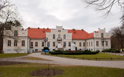 Pałac Przebendowskich w Wejherowie, z czerwonym dachem i kremową fasadą, otoczony zielenią i drzewami.