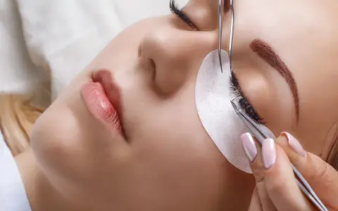 Une esthéticienne utilise des pinces pour appliquer des extensions de cils, une étape clé pour savoir comment coiffer ses sourcils et sublimer le regard.
