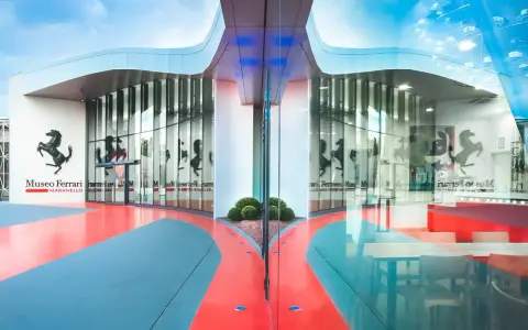 Nowoczesne muzeum Ferrari w Maranello, z charakterystycznym logo i odbijającymi się w szkle sylwetkami koni.
