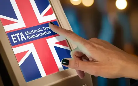 Dłoń dotyka ekranu z flagą Wielkiej Brytanii i napisem "ETA Electronic Travel Authorization". Czy do Londynu trzeba paszport? Sprawdź ETA.
