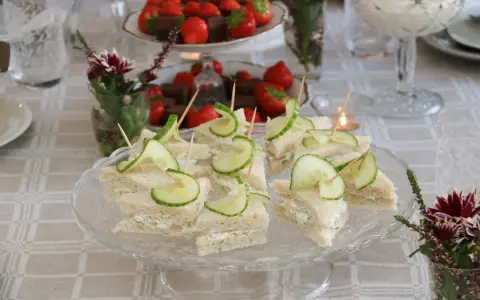 Smörgåsar med gurka och krämig fyllning, perfekta för ett afternoon tea recept. Jordgubbar och choklad i bakgrunden.
