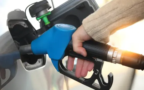Dłoń trzymająca niebieski pistolet do tankowania paliwa przy samochodzie.