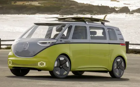 Volkswagen ID. Buzz w kolorze limonkowym z deskami surfingowymi na dachu, nad morzem.