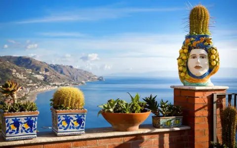 Balcone fiorito con vista sul mare, uno dei luoghi più belli della Sicilia. Cactus e piante grasse adornano la terrazza con vista sulla costa.