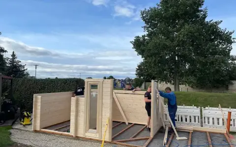 Männer bauen ein Gartenhaus. Die Montage schreitet voran, die Baugenehmigung ist hoffentlich vorhanden.