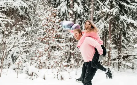 Szczęśliwa para w zimowym lesie, on niesie ją na barana, trzymają balony. Może to symbol tego, jak odzyskać partnera – wspólne chwile i radość.