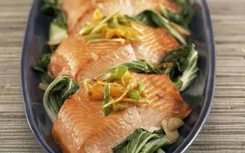 Saftiger Lachs mit Mangold, garniert mit Ingwer und Frühlingszwiebeln, auf einem dunkelblauen Teller serviert.