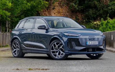 Elegancki, ciemnoniebieski Audi Q6 e-tron stoi na tle zieleni.