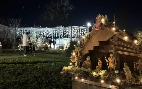 Bethlehemskrippe mit Figuren und Lichtern auf dem weihnachtsmarkt legden. Im Hintergrund eine Person mit Rollator und Lichterketten.