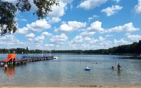 Sommerfreude im Strandbad Heiligensee: Kinder planschen, ein Mann kühlt sich ab, eine Rutsche lockt. Blauer Himmel mit weißen Wolken.