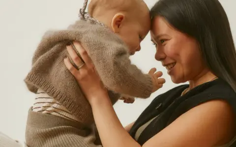 Madre y bebé se miran con ternura, frente con frente. El bebé, envuelto en un suéter de lana, muestra el apego infantil.