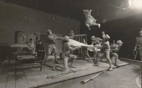 Scena teatralna: żołnierze w mundurach z epoki, jeden w powietrzu, trzymają białą tkaninę. Kantor Wielopole.