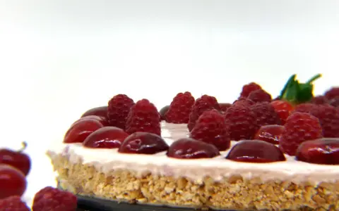 Cheesecake senza gelatina, guarnita con lamponi succosi e ciliegie lucide, su una base croccante.