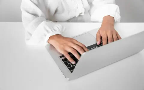 Osoba w białej koszuli pisze na laptopie, przygotowując zaświadczenie o niezaleganiu ZUS.