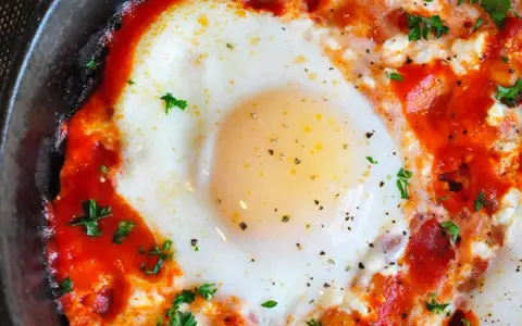 Uova al pomodoro, un piatto saporito con uovo cotto in salsa di pomodoro e formaggio, guarnito con prezzemolo fresco.