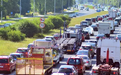 Korek na drodze, sznur samochodów i ciężarówek. Widać znak ograniczenia prędkości do 70. Może to być sytuacja wymagająca polisa car.
