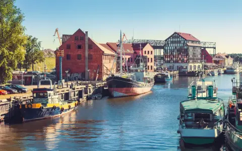 Barche ormeggiate nel porto di Klaipeda, Lituania, con edifici storici e gru sullo sfondo.