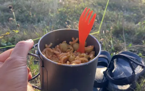 Un repas simple pour savoir que manger en randonnée : des pâtes avec des olives dans une tasse de camping, avec une fourchette orange.