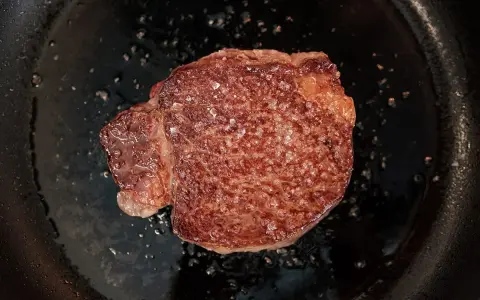 Ein saftiges Steak brutzelt in der Pfanne, bestreut mit grobem Salz.