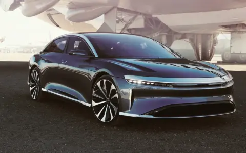 Ciemny sedan Lucid Air na tle samolotu.