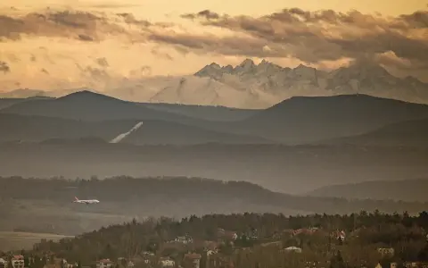 Widok na Tatry z Krakowa. Samolot leci nad mglistymi wzgórzami, a za nimi widać ośnieżone szczyty.