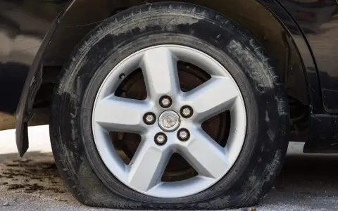 Ruota sgonfia dell'auto, con cerchione in lega a cinque razze e pneumatico sporco.