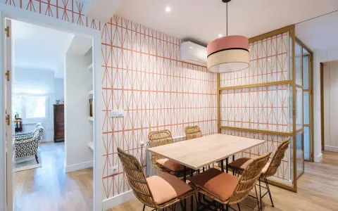 Comedor con papel pintado de rombos naranjas, mesa de madera y sillas de mimbre. Un ejemplo de como poner papel pintado para renovar tu hogar.