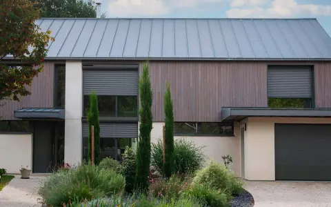 Façade moderne avec volet roulant maison ancienne, bois, pierre et jardin luxuriant.
