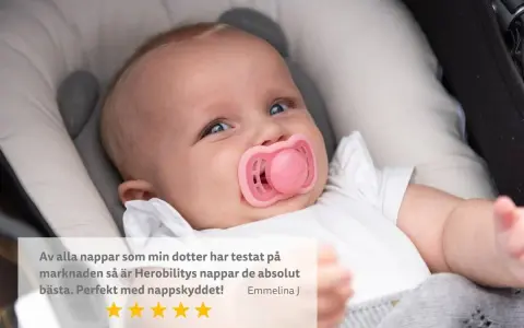 Söt bebis med rosa napp i munnen, som verkar nöjd. En recension lyfter fram nappens kvalitet.