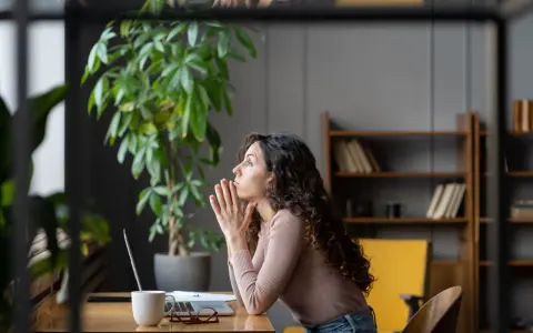 Mujer pensativa en su escritorio, con las manos juntas, reflexionando sobre sus permisos retribuidos.